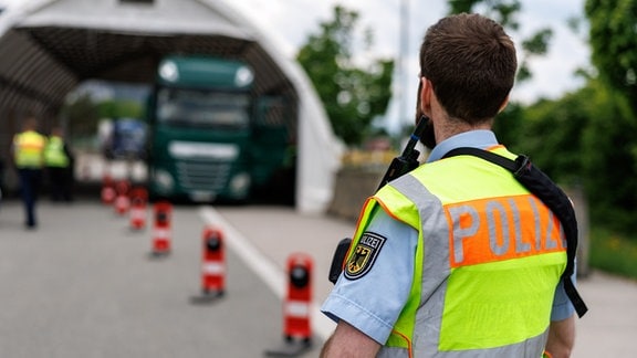 Ein Polizist sichert an der deutschen Grenze die Kontrollstelle auf einer Raststätte, in der ein gestoppter Lastwagen steht.