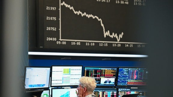 Eine Börsenhändlerin beobachtet auf dem Parkett der Frankfurter Wertpapierbörse ihre Monitore, während die Anzeigetafel mit der Dax-Kurve fallende Kurse anzeigt.