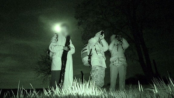 Acktivisten in der Dämmerung auf einem Feld vor der Anlage