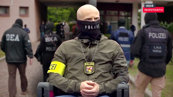 Ein Polizist mit Maske. Dahinter weitere Polizisten bei einem Einsatz