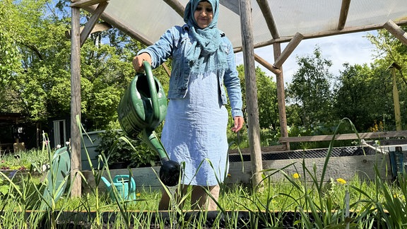 Eine Frau aus Kabul steht an einem Gartenbeet und gießt Gemüsepflanzen.