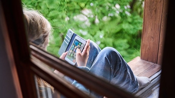 Ein Junge sitzt am Fenster und schaut auf sein Handy
