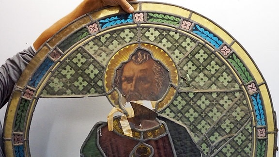 Buntes beschädigtes Kirchenfenster wird von einer Person gehalten.