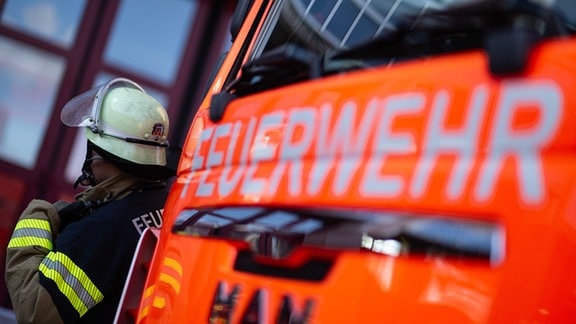 Eine Einsatzkraft der Feuerwehr steht neben einem Einsatzfahrzeug der Feuerwehr.
