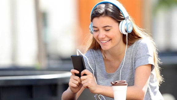 Junge frau hört am Handy Musik mit Kopfhörern.