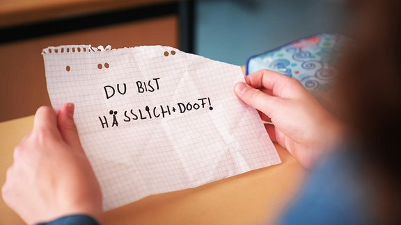 Ein Schüler liest einen Zettel auf dem steht "Du bist hässlich und doof"