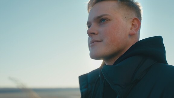 Eine Person mit dunkler Jacke vor einem blau-weißen Himmel.