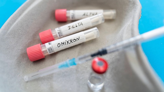 Ampullen mit Aufschrift: "Alpha", "Delta" und "Omikron" sowie Spritze